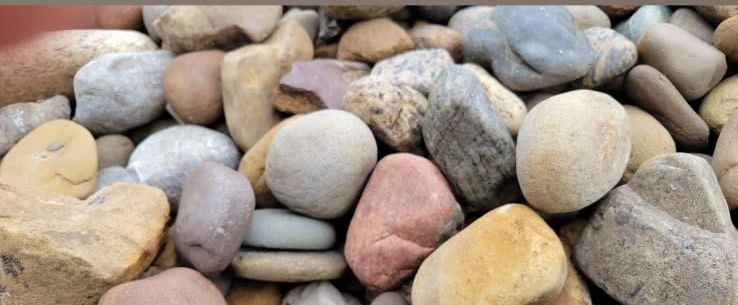 A dense band of smooth multicoloured river rock in tan, pink, grey and blue