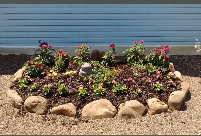 A small garden bed edged in natural stone against light blue siding