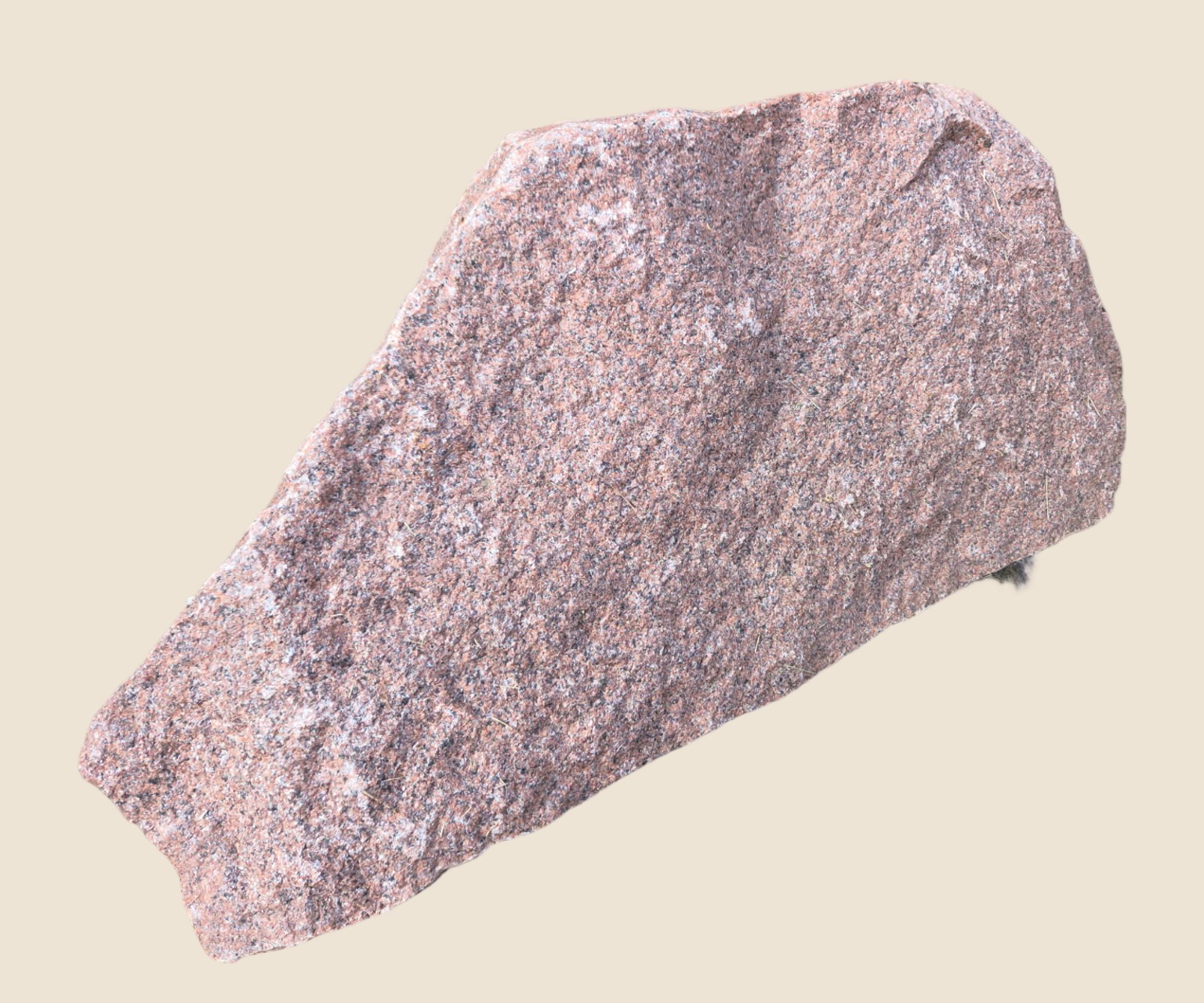 The whole pink speckled granite slab shown uncropped on a plain sand ground